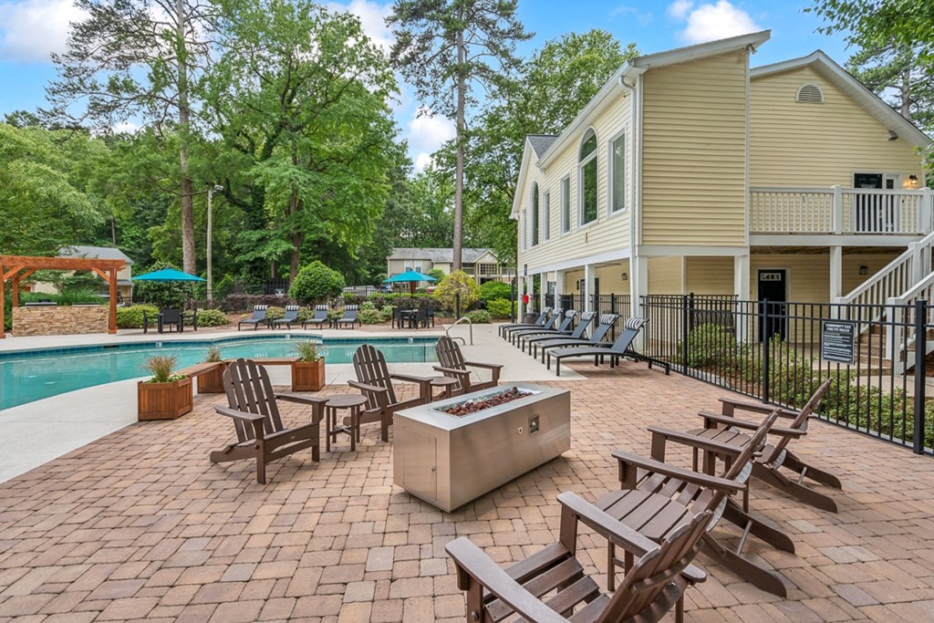 a backyard with a pool and patio with chairs and umbrellas