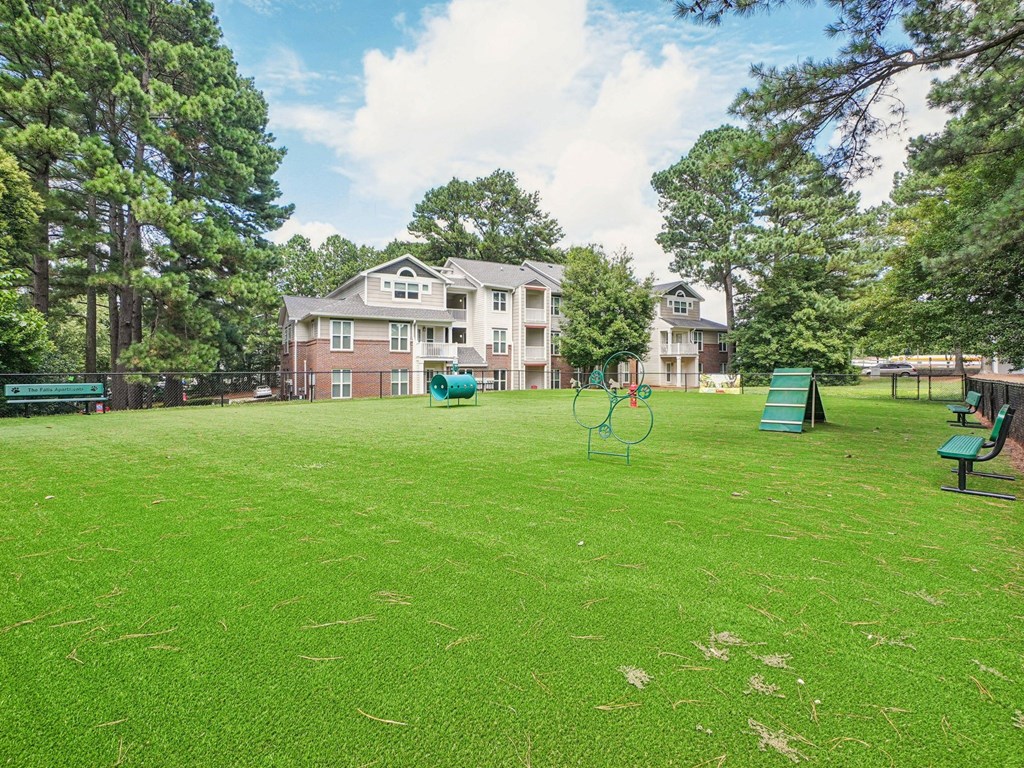 A grassy field with a playground and apartment buildings in the background at The Falls Apartments in Raleigh NC