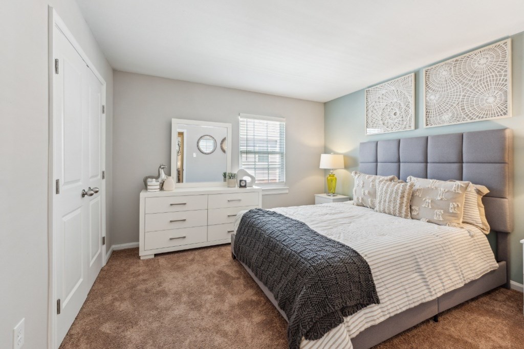 A bedroom with a bed, dresser, and mirror at Staples Mill Townhomes Apartments, Virginia