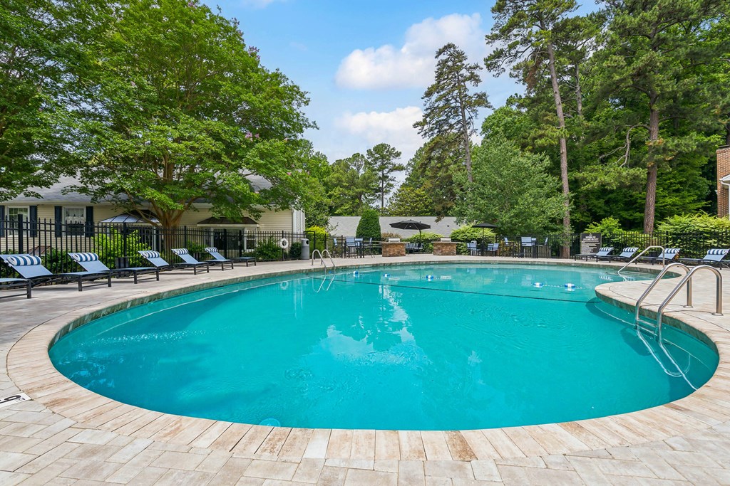 a swimming pool with chairs around it and trees in the background