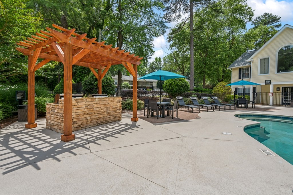 a backyard with a pool and a wooden pavilion with tables and umbrellas
