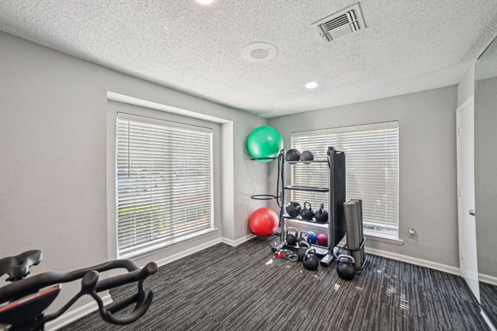 A room with a variety of exercise equipment including a stationary bike, a rowing machine, and a set of dumbbells at Willow Ridge Apartments, North Carolina, 28210