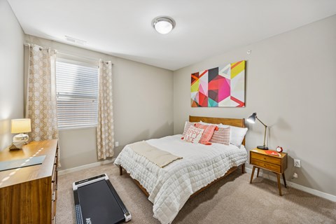 A bedroom with a bed, nightstand, and a painting on the wall.