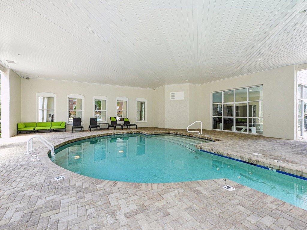 A large indoor swimming pool with a tiled floor and a bench at The Falls Apartments in Raleigh NC