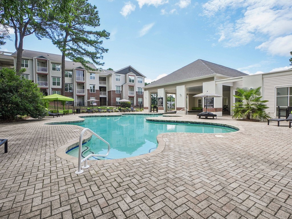 A swimming pool surrounded by a brick patio and apartment buildings at The Falls Apartments in Raleigh NC
