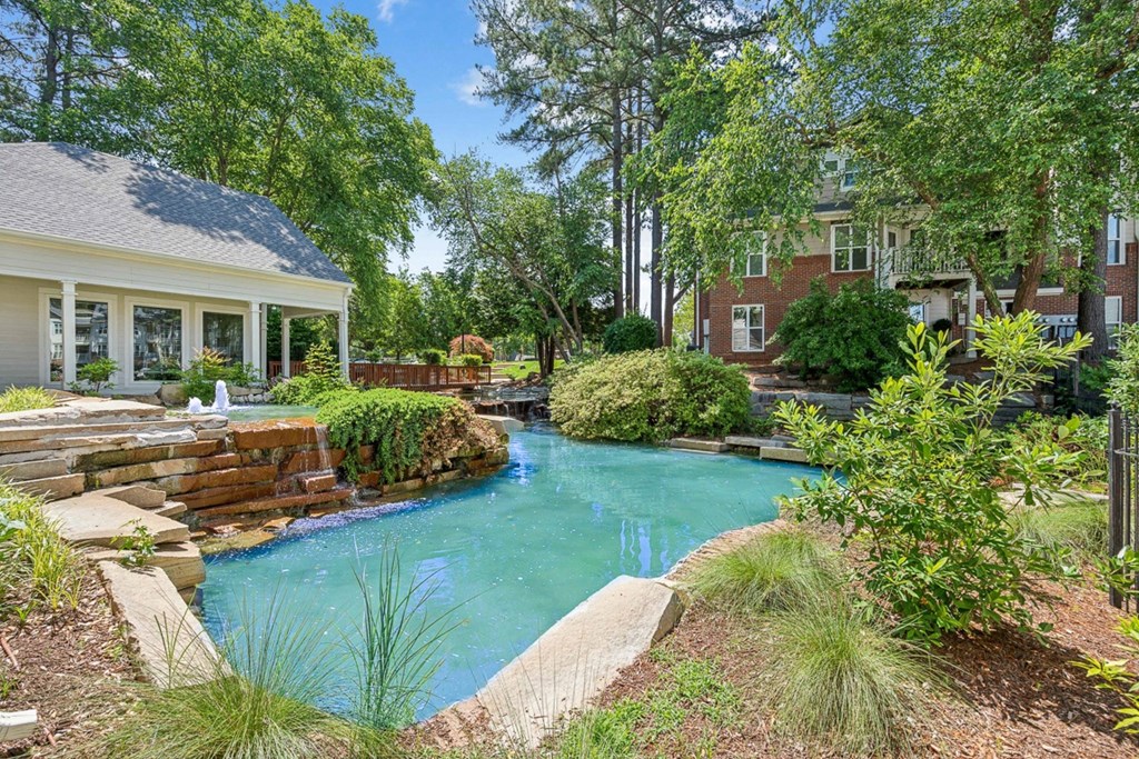 a swimming pool with a waterfall in front of a house at The Falls Apartments in Raleigh NC