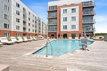 A large swimming pool is surrounded by lounge chairs in a courtyard.