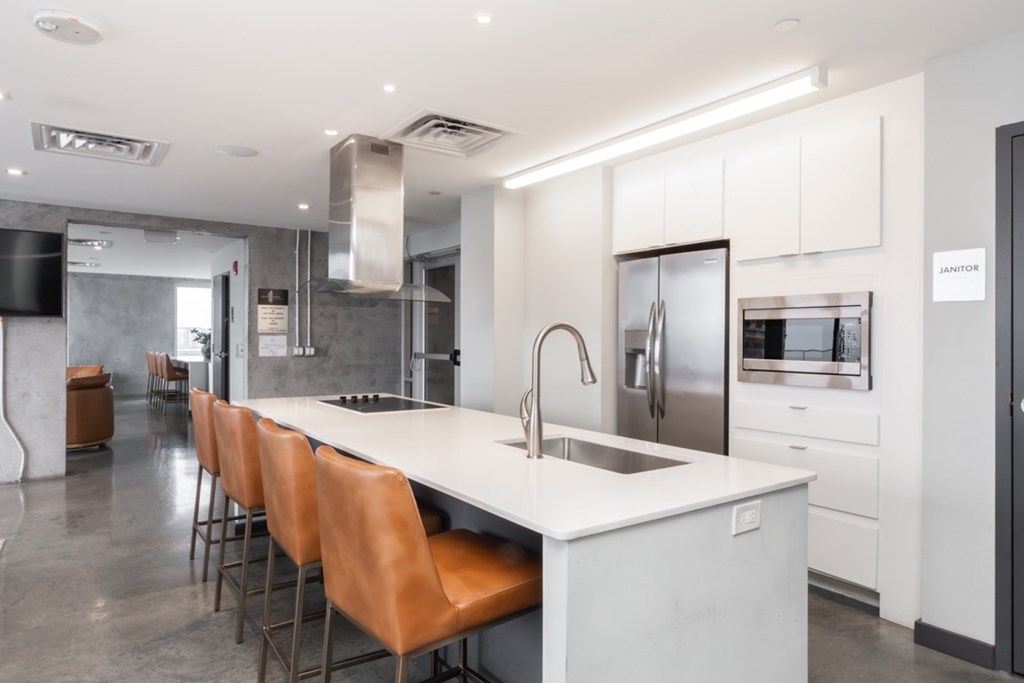 A modern kitchen with a long white island and brown chairs.