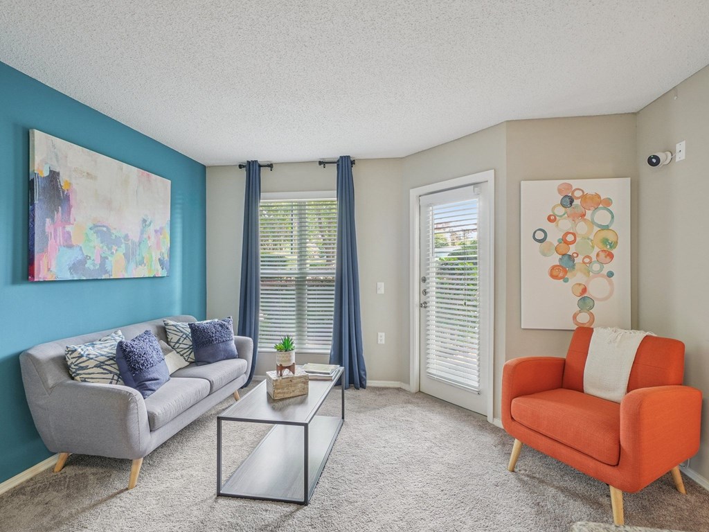 A living room with a grey couch, a red chair, and a glass coffee table at The Falls Apartments in Raleigh NC