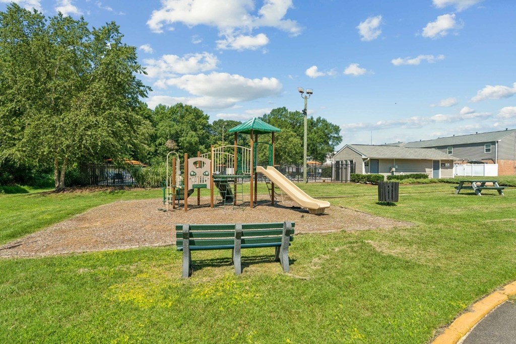 A playground with a green slide and two benches at Staples Mill Townhomes Apartments, Richmond 23228