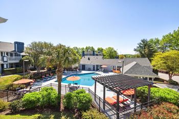 an aerial view of a pool with umbrellas and a building in the background at Palmetto Place Apartments, Taylors, SC, 29687