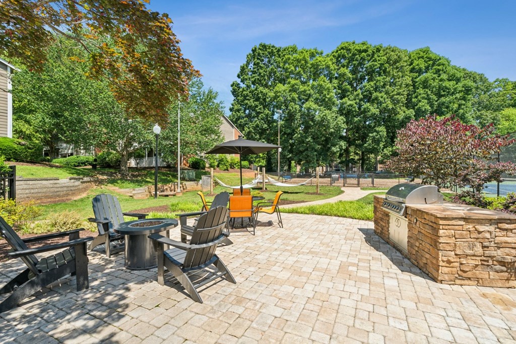 A patio with chairs and a table is surrounded by trees at Woodcreek Apartments, Cary, 27511