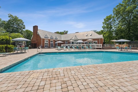A large outdoor swimming pool with a brick patio and a house in the background. at The Timbers Apartments, Virginia
