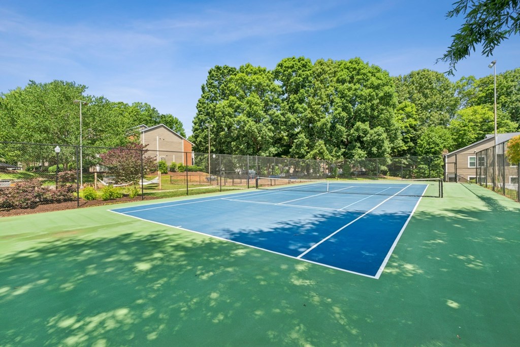 A tennis court surrounded by trees and a fence. at Woodcreek Apartments, North Carolina, 27511