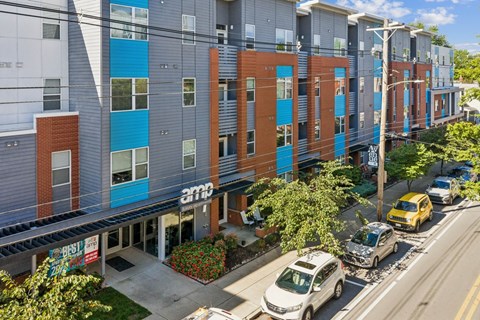 A street view of a row of apartment buildings with cars parked on the street.