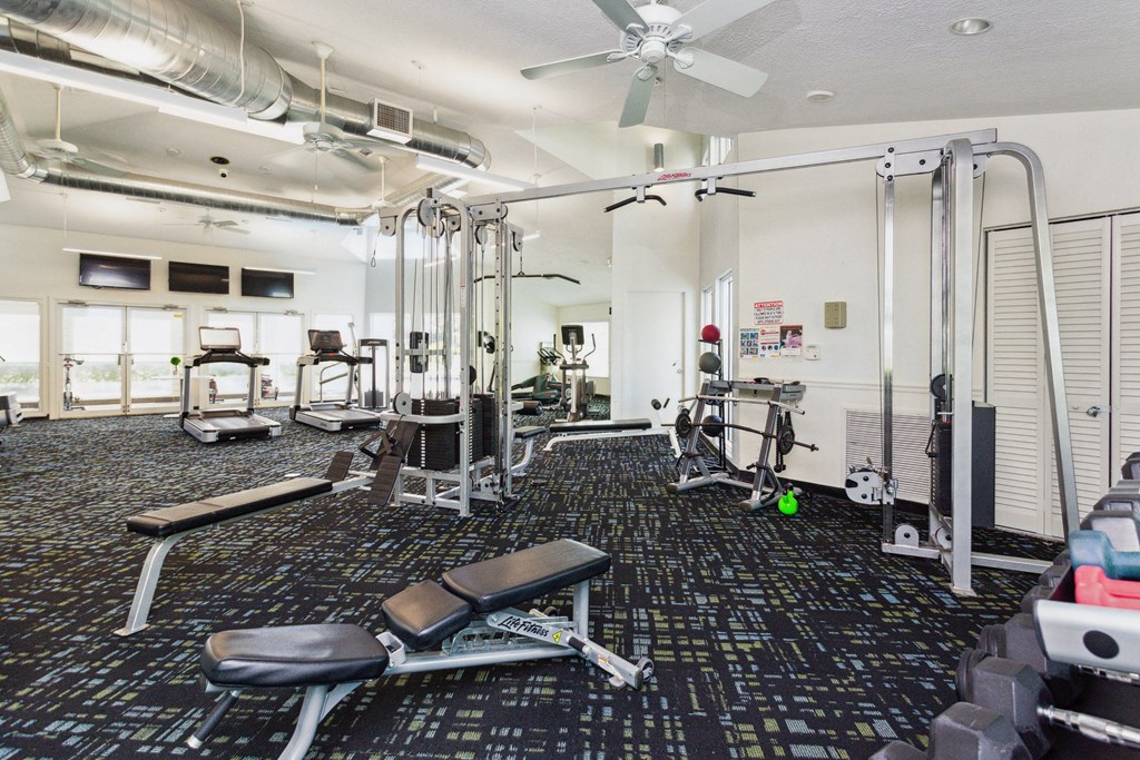a gym with cardio equipment on the floor and a ceiling fan