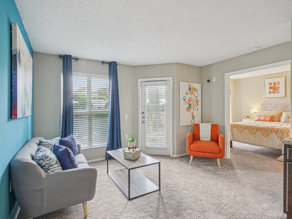 A living room with a grey couch, a glass table, and a red chair at The Falls Apartments in Raleigh NC
