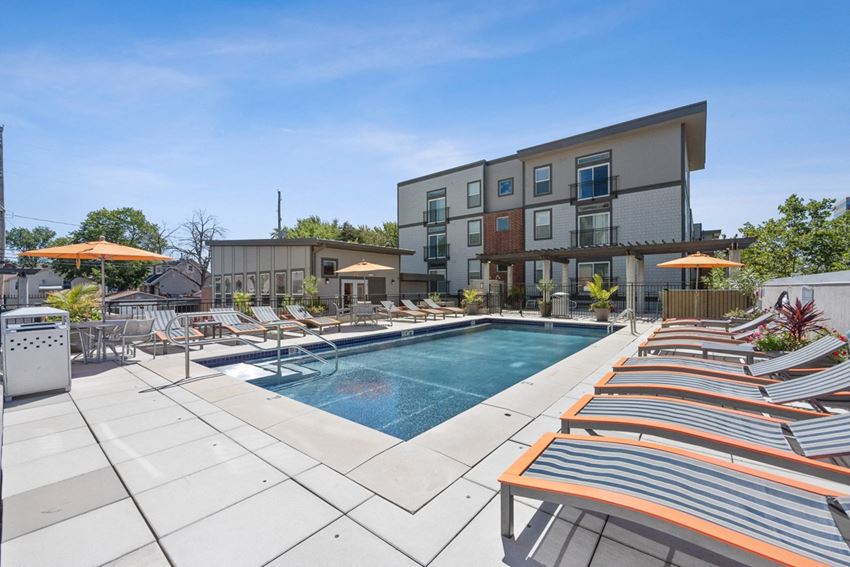 Swimming Pool with Chaise Lounge Chairs a swimming pool with chaise lounge chairs and umbrellas in front of a building