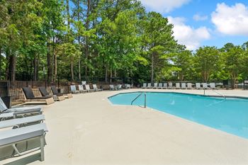 A pool surrounded by trees and lounge chairs.