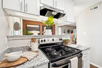 A modern kitchen with a stove top oven and a cutting board with a bowl and utensils on it. at Woodcreek Apartments, Cary