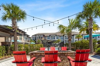 a patio with red chairs and a fire pit with palm trees at The Loree, Jacksonville, 32256