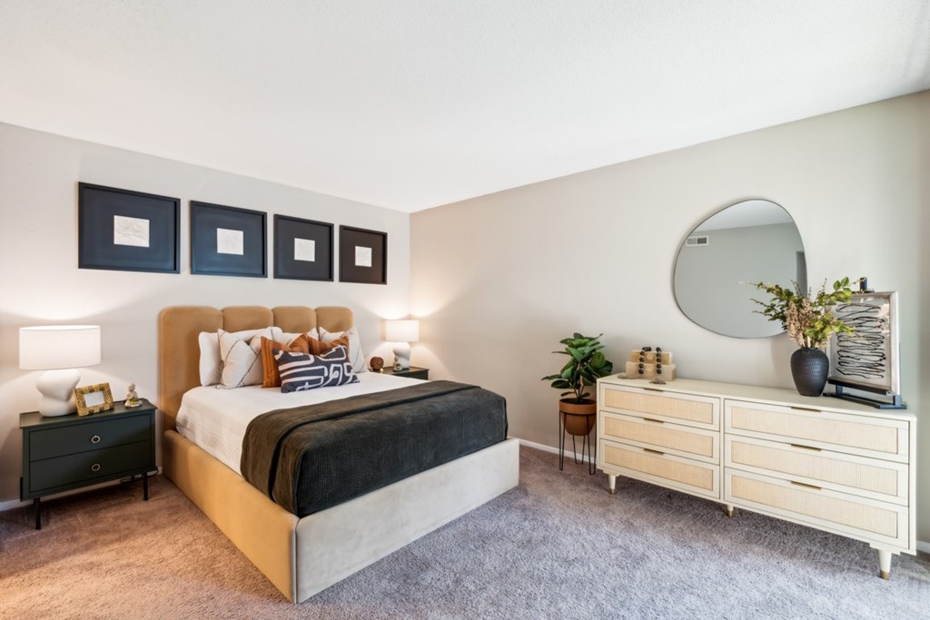 A bedroom with a large bed, a dresser, and a mirror. at Woodcreek Apartments, Cary, North Carolina