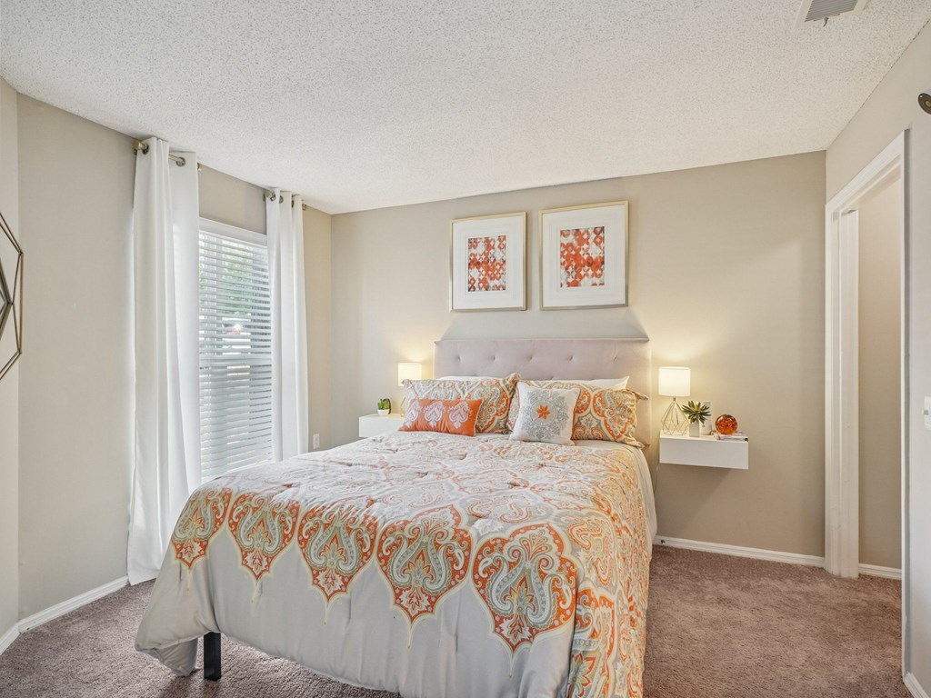 A bedroom with a bed, two pillows, a nightstand, and two framed pictures on the wall at The Falls Apartments in Raleigh NC