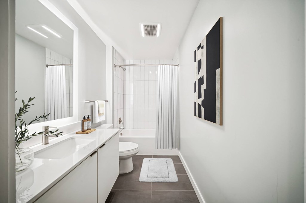A bathroom with a white sink, toilet, and bathtub with a grey floor and a white wall.