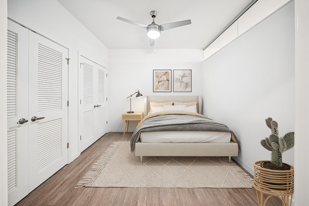 A bedroom with a bed, a cactus, and a ceiling fan.