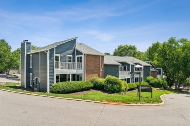 A modern two-story building with a grey and brown exterior and a landscaped front yard. at Woodcreek Apartments, North Carolina