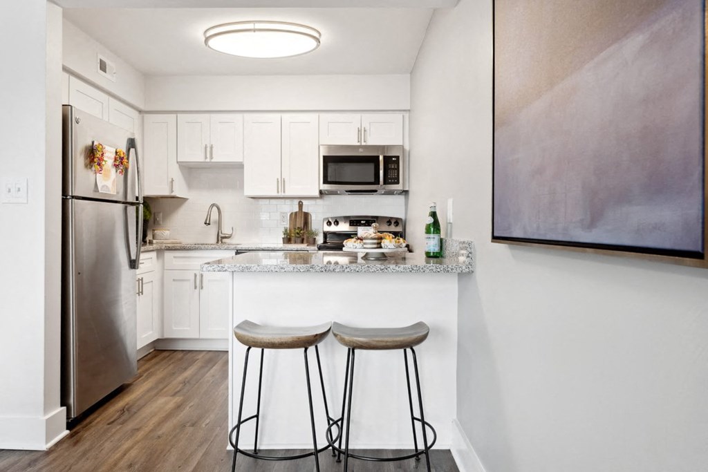 a kitchen with white cabinets and a small island with two stools at Linkhorn Bay Apartments, Virginia Beach