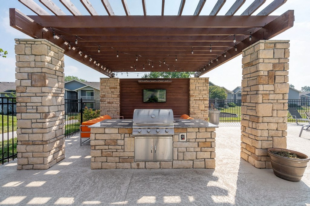 an outdoor kitchen with a grill and a tv under a pergola at The Reserve At Barry Apartments, Kansas City, Missouri