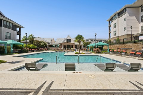 A large swimming pool with lounge chairs and umbrellas in front of apartment buildings.