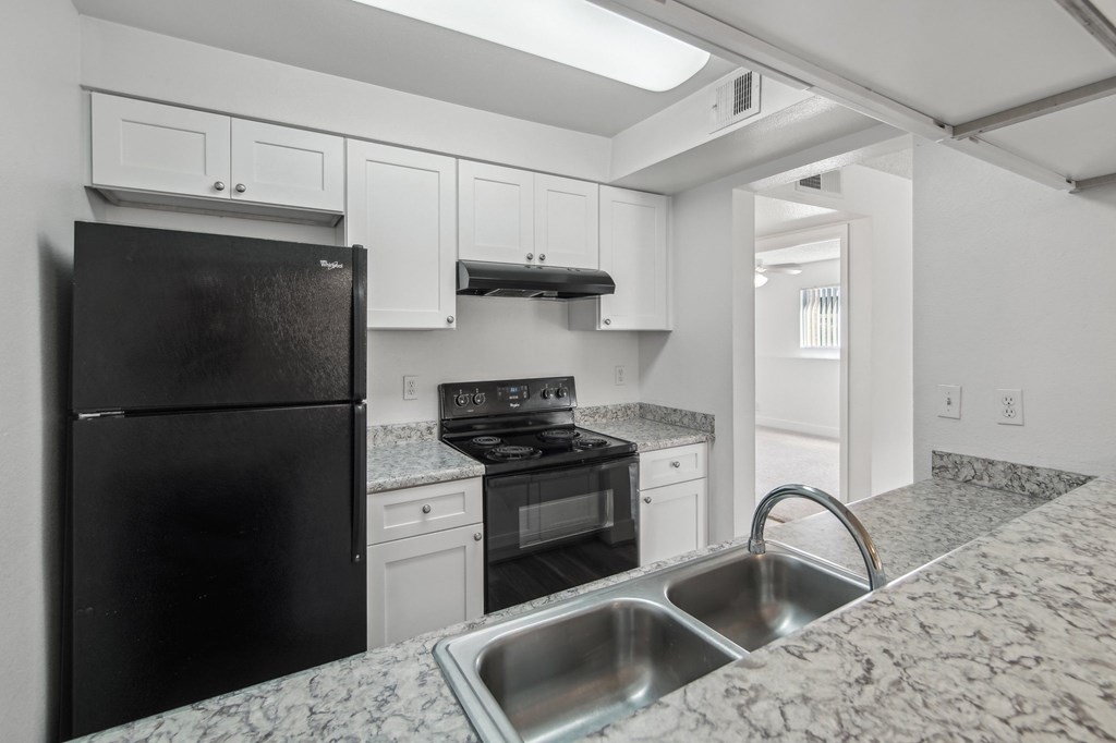 A black refrigerator is in a kitchen with granite countertops at Candela Park Apartments, Mesa