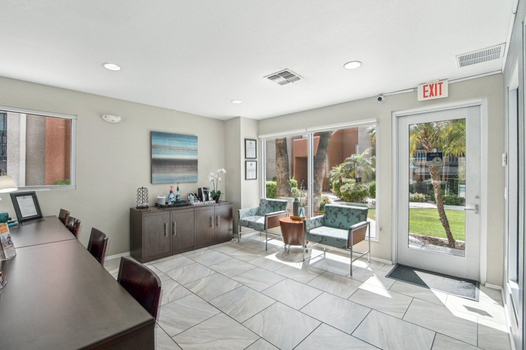 A conference room with a long table and chairs, a framed picture on the wall, and a view of the outside through the glass door at Candela Park Apartments, Mesa, Arizona