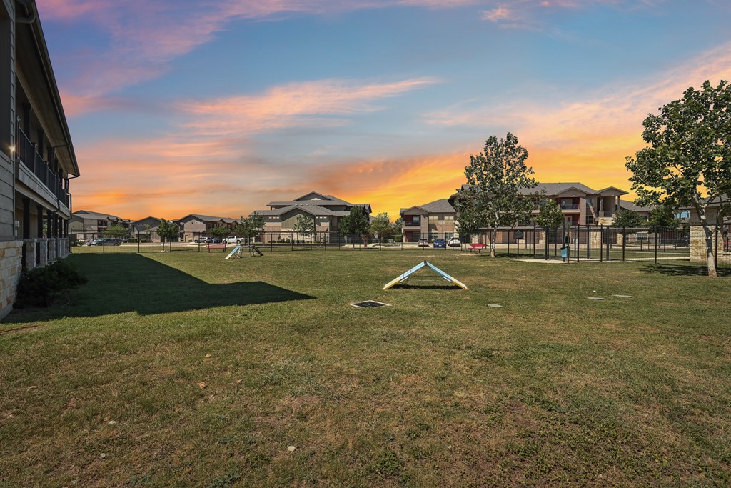 A sunset view of a park with a playground and houses in the background.