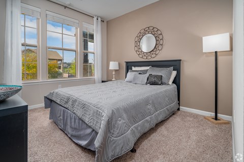 A bedroom with a large bed and a window overlooking a house at Overlook at Stone Oak Park Apartments, San Antonio