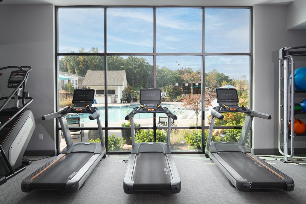 a gym with cardio equipment and a window view of a swimming pool