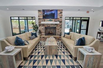 Clubhouse fireplace lounge with large TV, two sofas, coffee tables, and a modern rug near windows - Photo Gallery 11