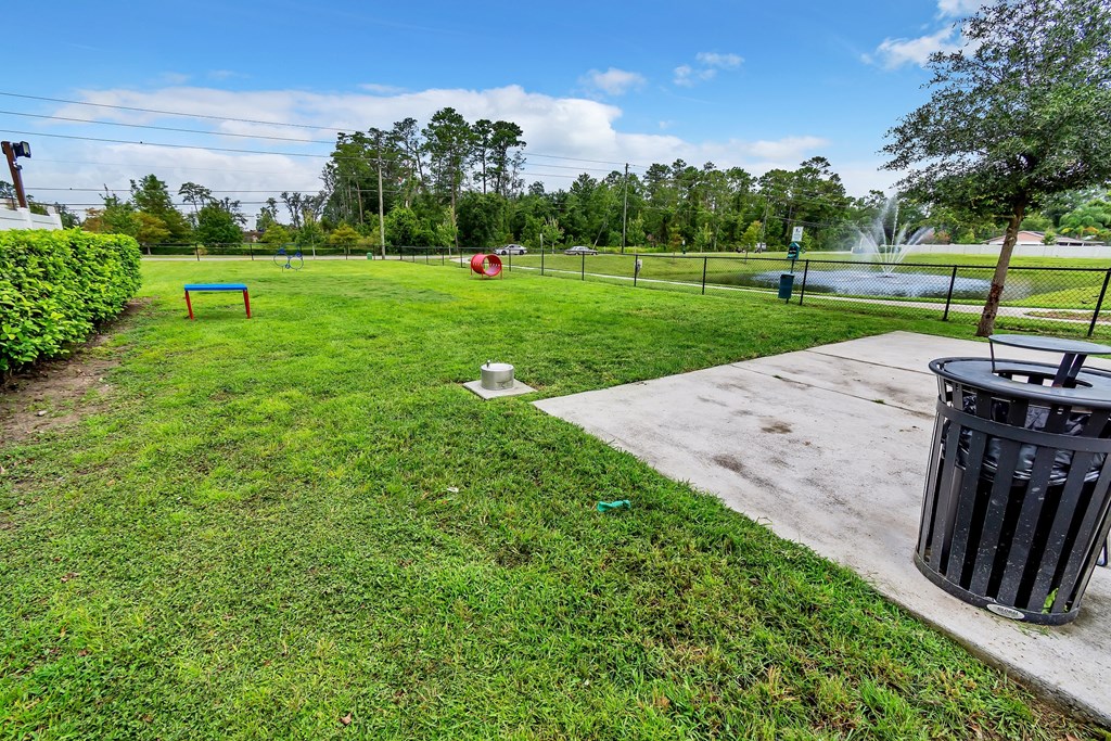 a grassy area with a trash can and a bench