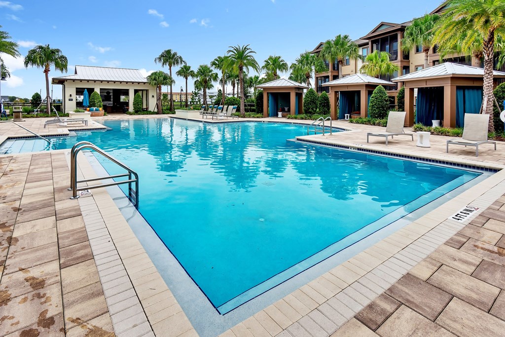 a resort style swimming pool with lounge chairs and palm trees in the background