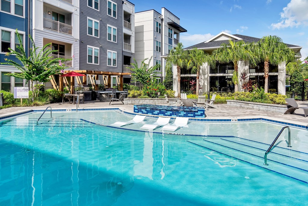 a swimming pool with lounge chairs and umbrellas in front of an apartment building