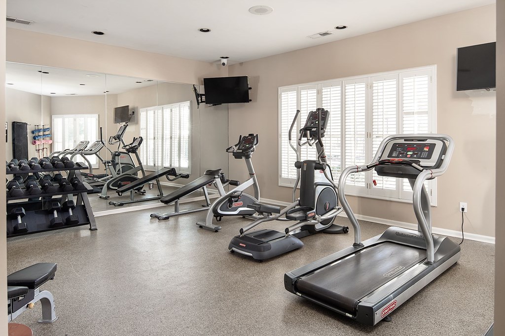 A spacious home gym with treadmills, elliptical machines, and a television.