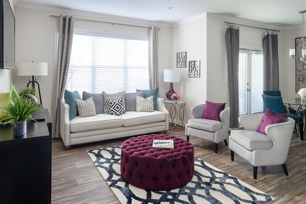 A living room with a white couch, two chairs, and a red ottoman.