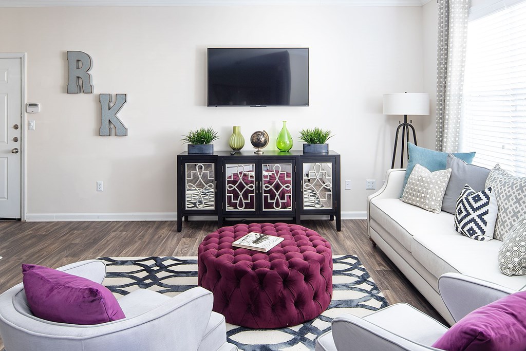 A living room with a white couch, a red ottoman, and a TV mounted on the wall.