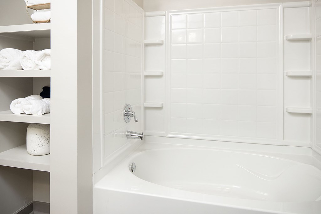A white bathroom with a tub and towel shelf.