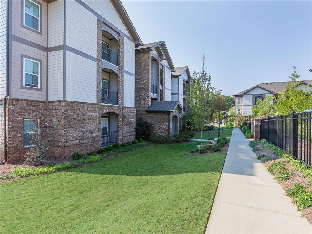 A long concrete walkway leads to a brick building with a black fence on the right.