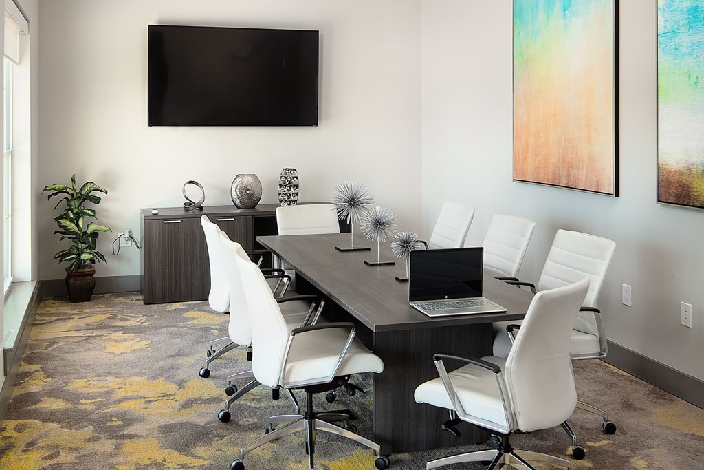 A conference room with a long table and chairs, a laptop on the table, and a TV mounted on the wall.