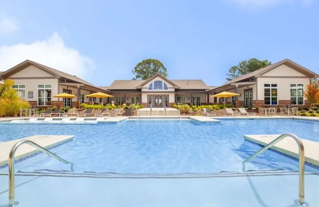 A large swimming pool in front of a building with a yellow umbrella.