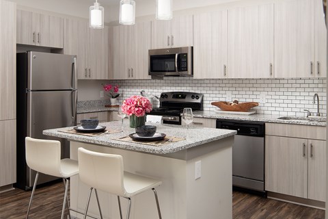 A kitchen with a refrigerator, microwave, oven, sink, and a counter with two chairs.